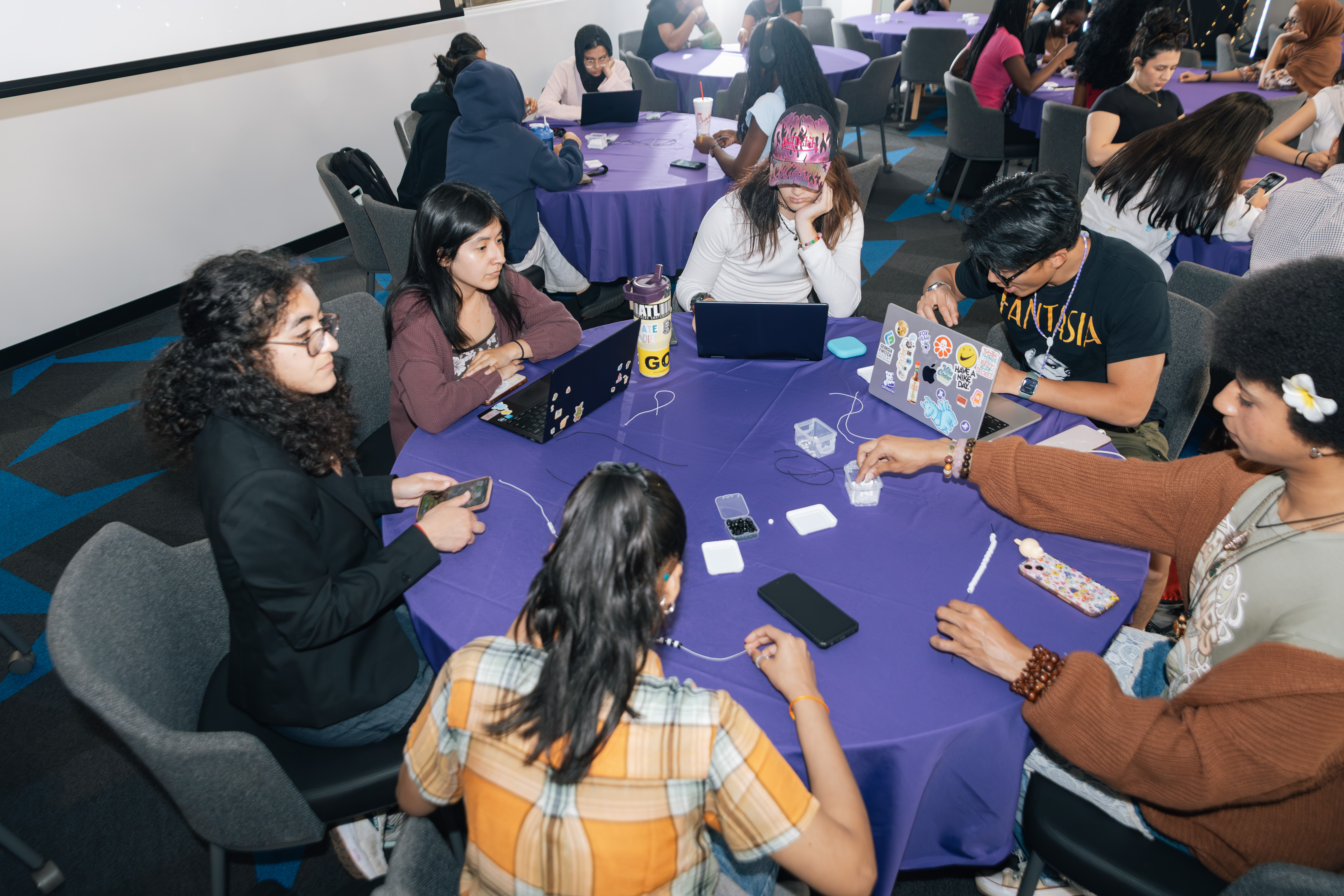 progirls members collaborating around a table with laptops and craft supplies at a buildnight